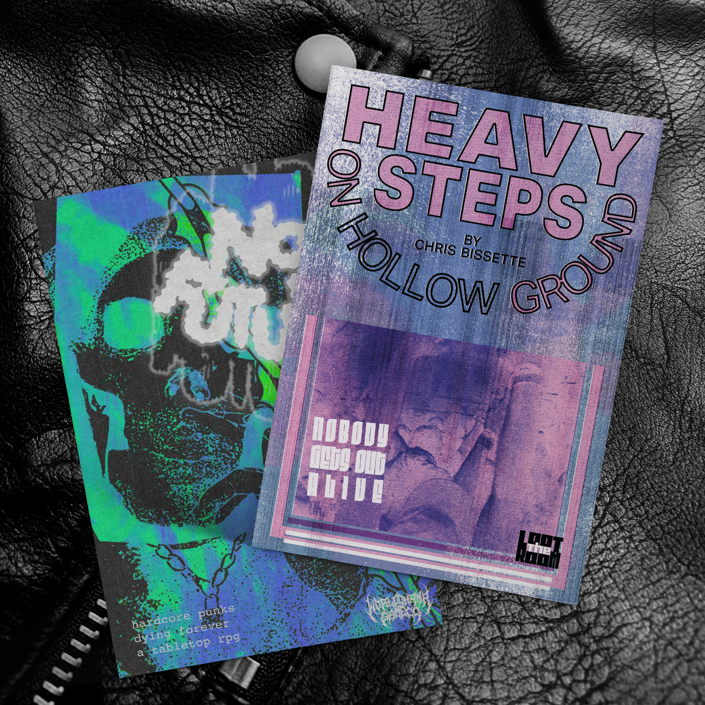 A pair of softcover zines sitting on a leather background. One is pink and purple and has the title "Heavy Steps On Hollow Ground". The other is green and blue and has the title "No Future".